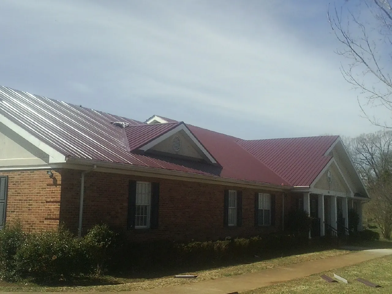 Red metal roof with gabled entries on a long brick building, from a Hail Damage Roof Repair job in Underwood