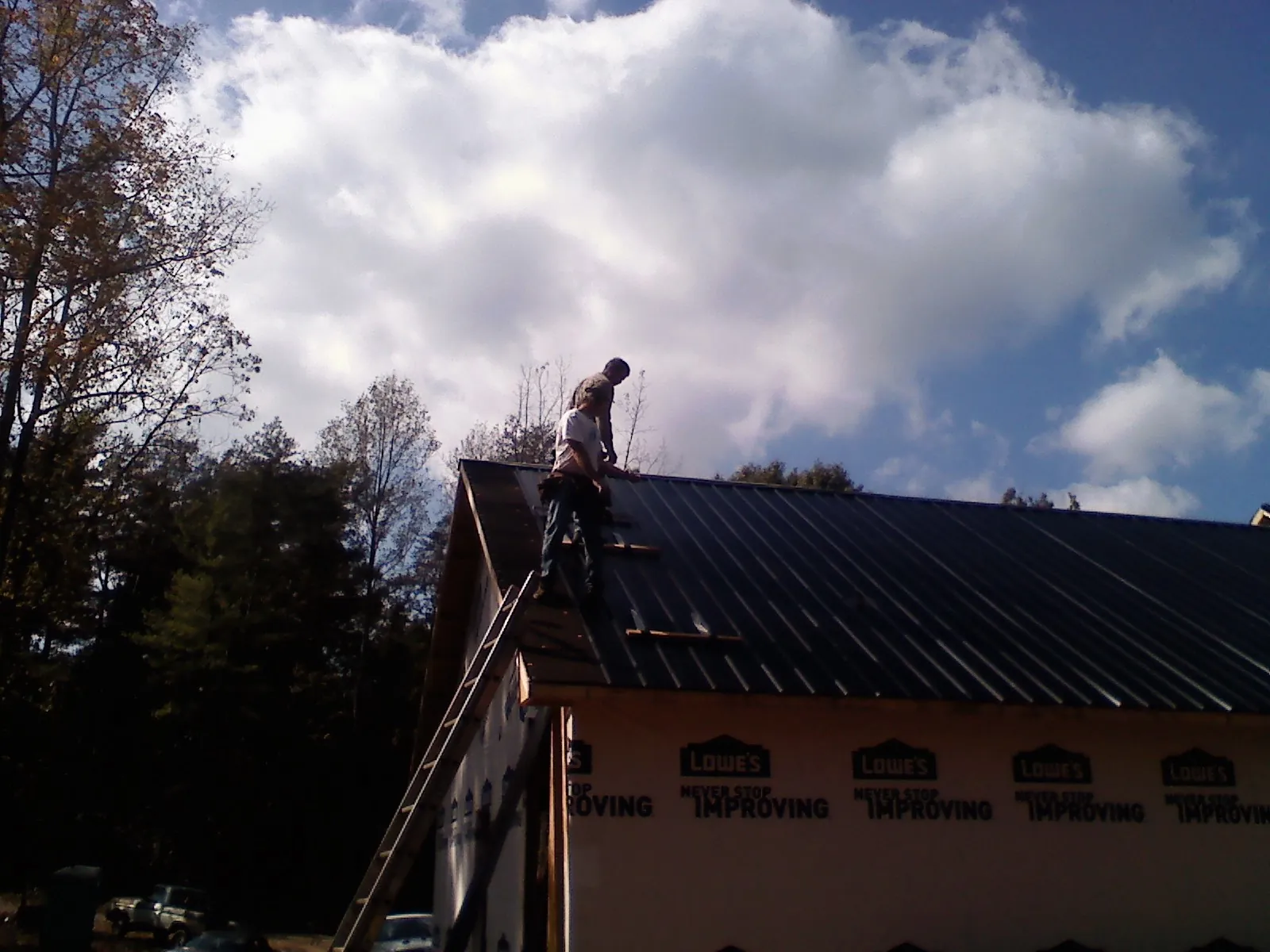 Roofer fastening dark metal panels high against a cloudy sky, from a Roof Inspection job in Underwood