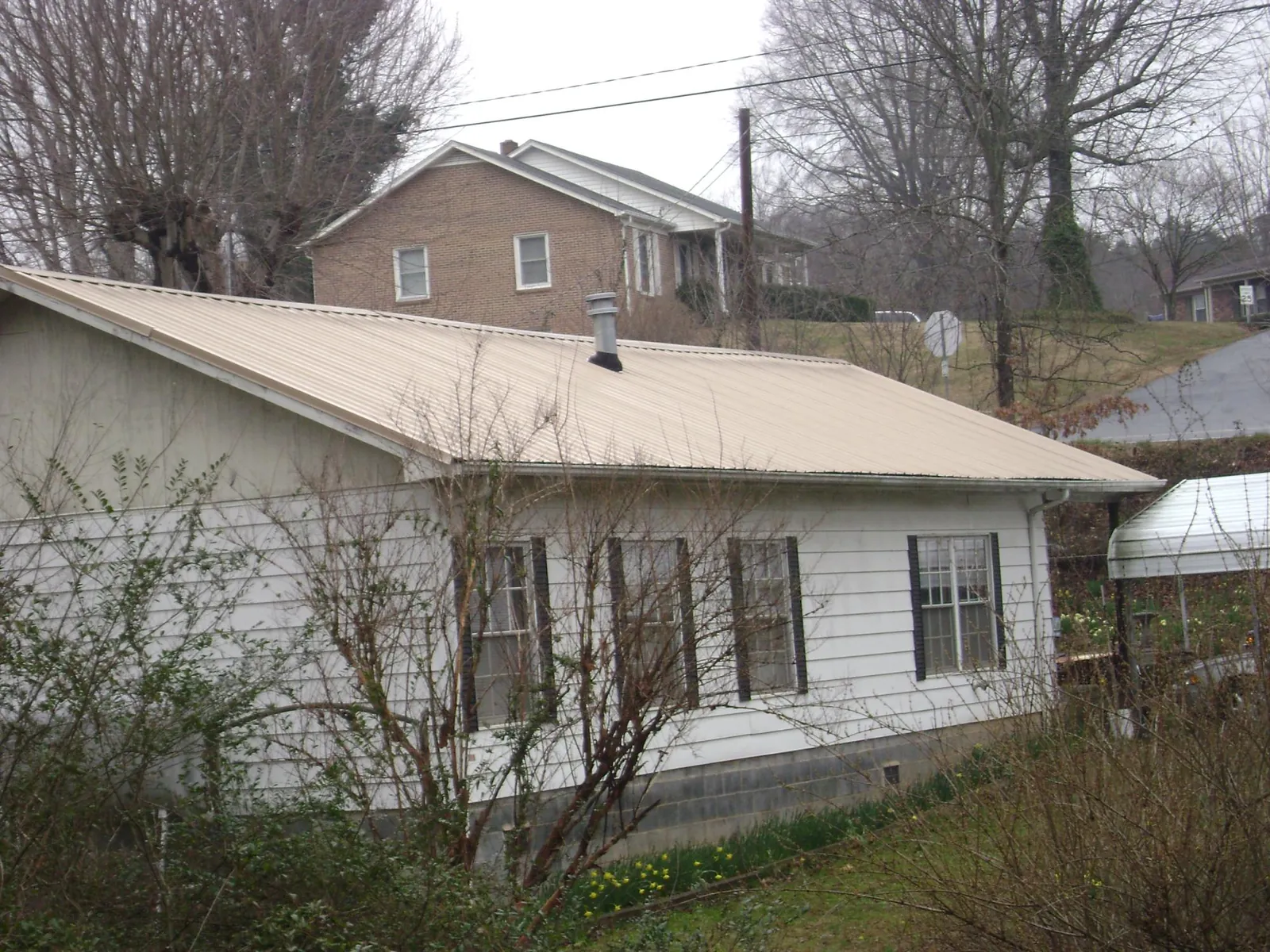 Tan metal roof on a white sided house set into a hillside — Commercial Roofing by Roofing Brothers in Underwood